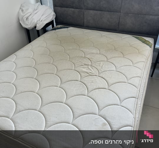 מזרן עם כתמים על רצפת אריחים ליד חלון